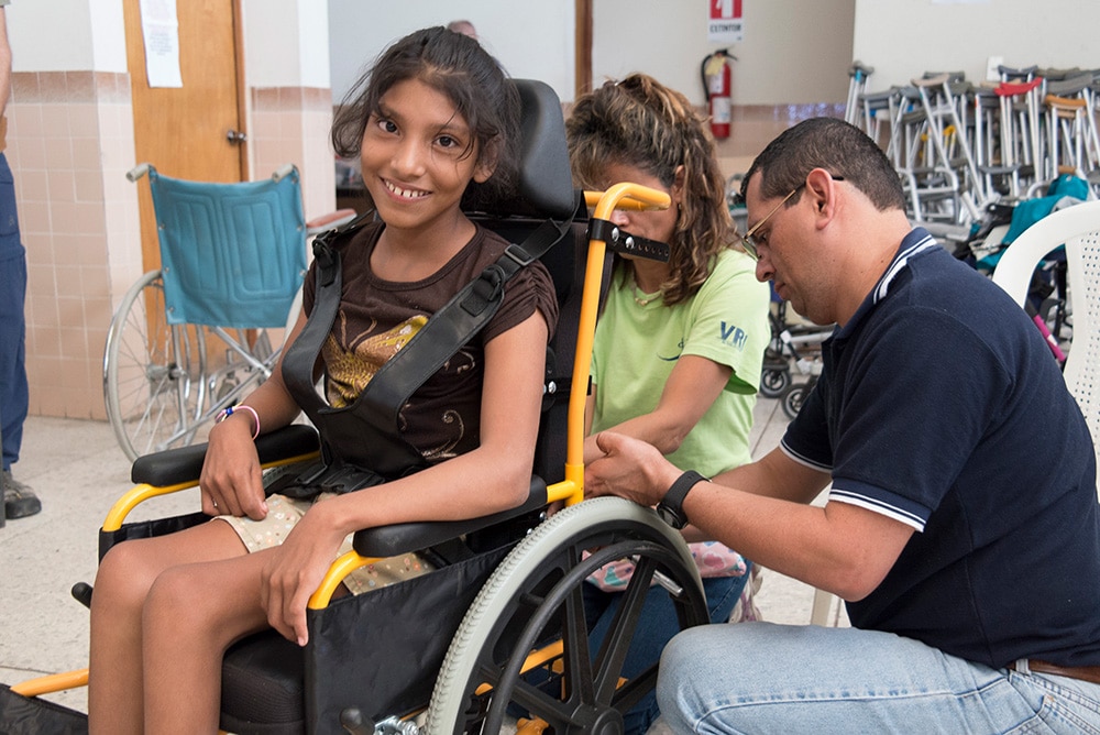 A child in a wheelchair smiles are her wheelchair is being adjusted