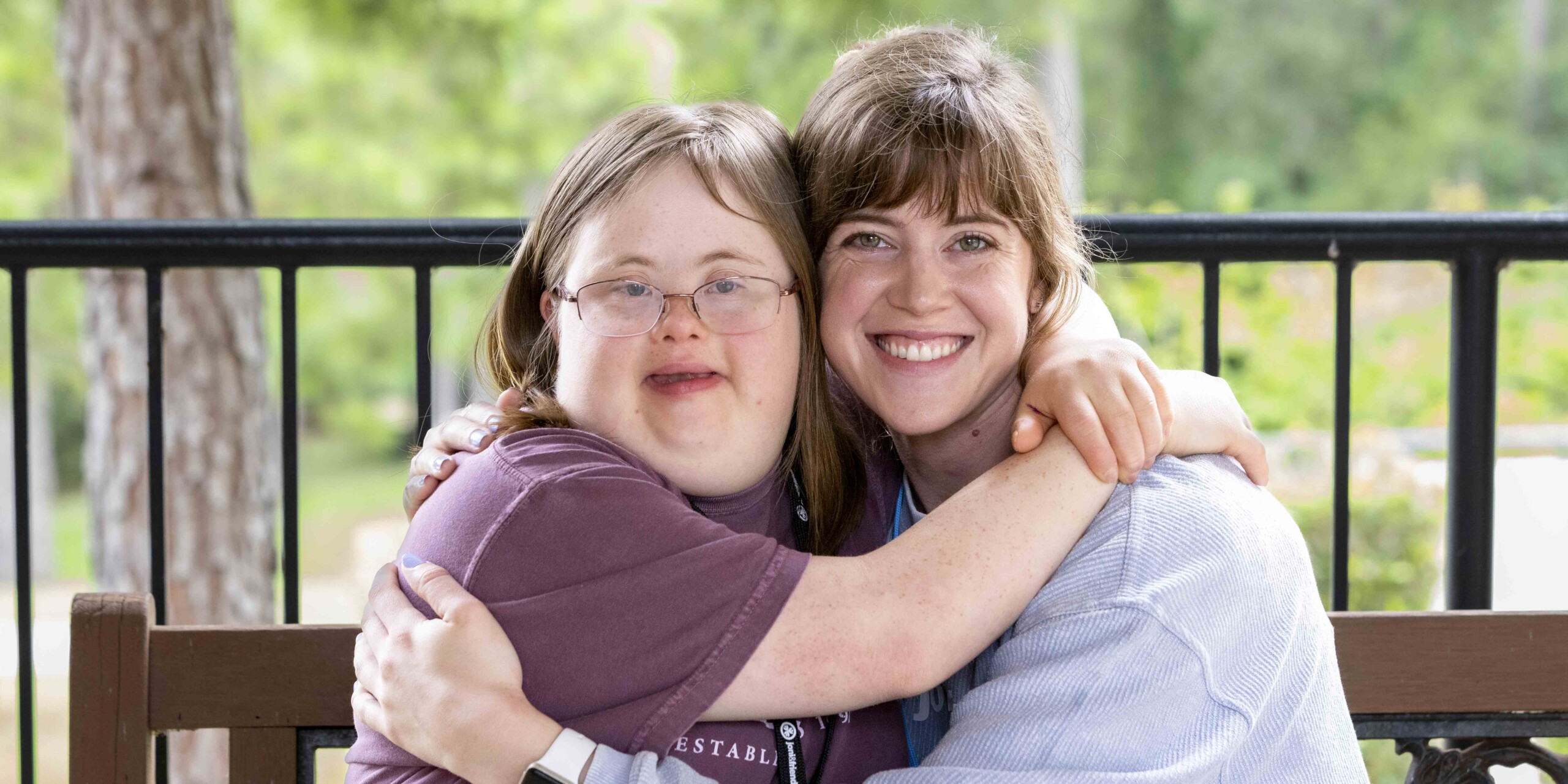 A woman hugging a girl with Down syndrome; both are smiling at the camera.