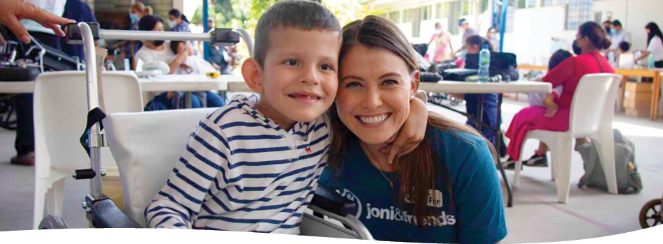 A volunteer with a boy smiling in his wheelchair.