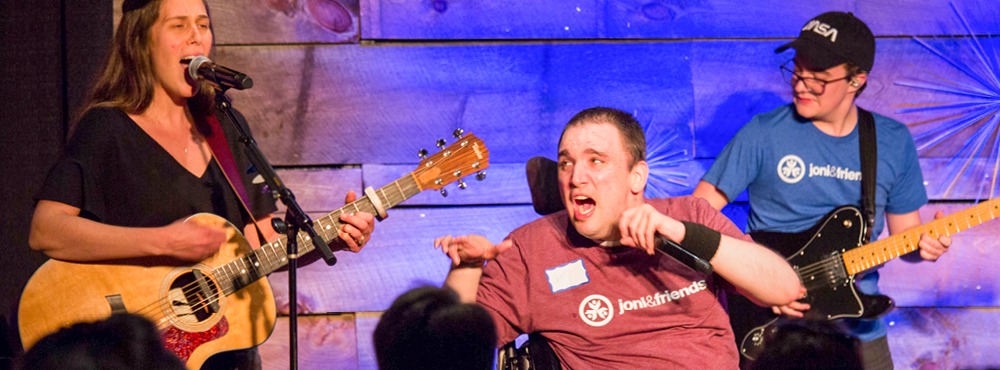 A group of worship leaders (some with disabilities) praising God on stage.