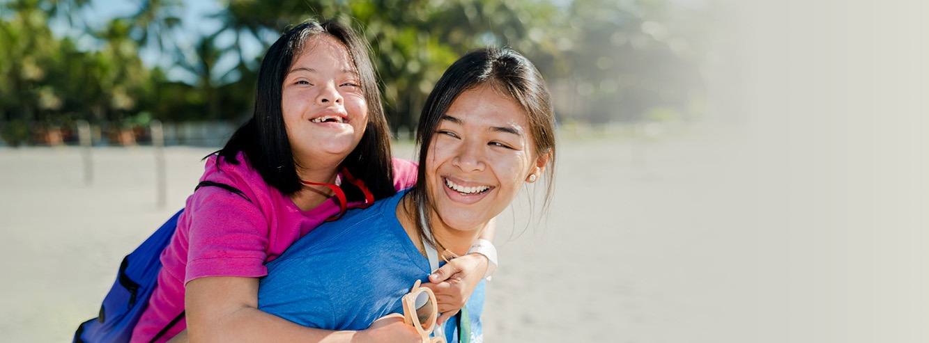A smiling intern gives a beaming child a piggy back ride.